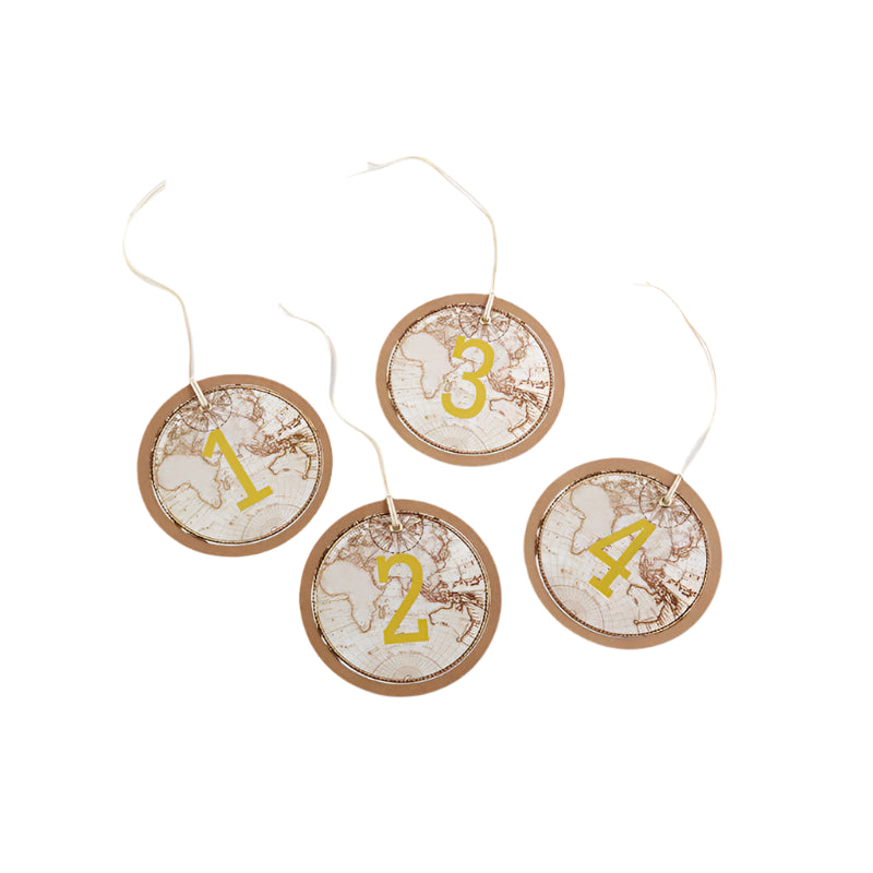 Four round kraft cardstock table numbers with a vintage-inspired map design and gold foil numbers, placed on a white surface.