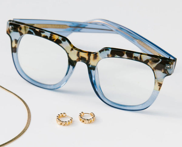 Blue and tortoiseshell glasses with gold hoop earrings on a light gray background