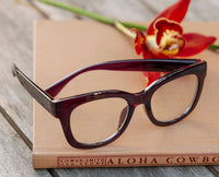 Dark cherry eyeglasses on a book with a red flower in the background