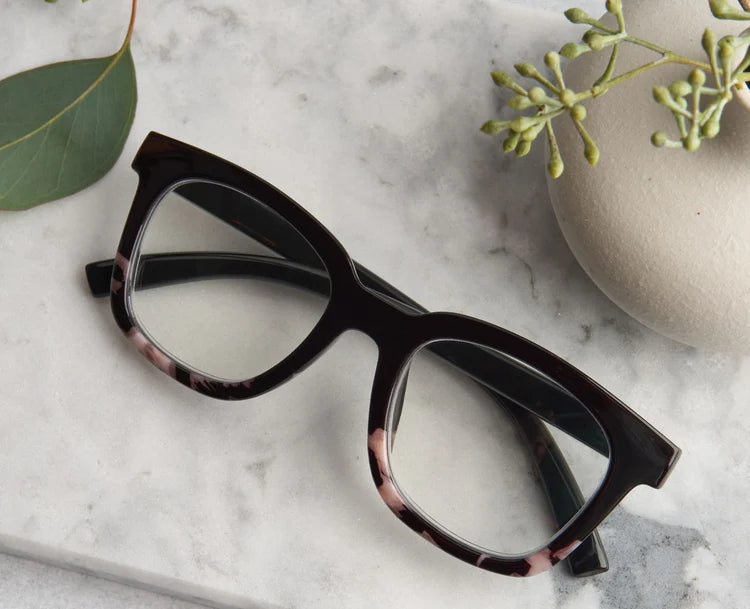 Black eye glasses with marble accents on a marble surface with green leaves