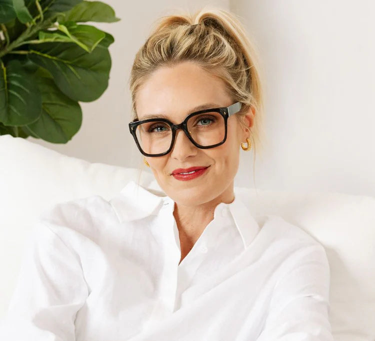 Woman wearing glasses and a white shirt with a plant in the background