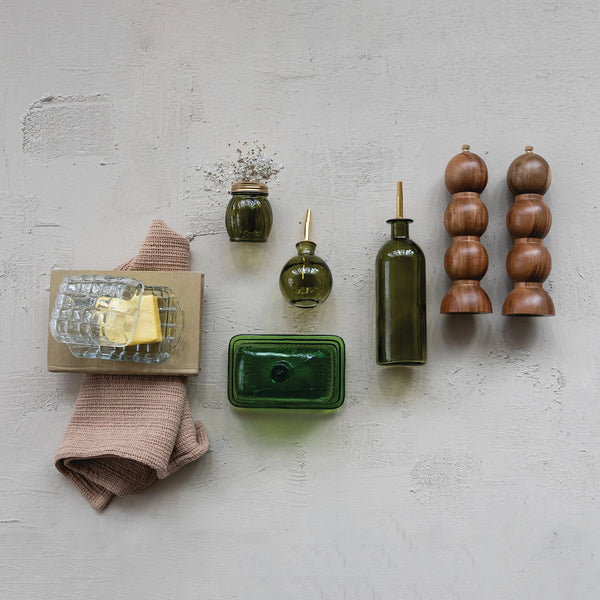 Collection of kitchen items including a green bottle, wooden salt and pepper shakers, and a pink towel on a light gray surface.
