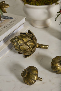 Gold artichoke-shaped objects on a marble surface with books and a white vase in the background.
