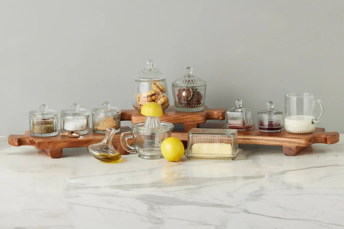Set of glass jars and containers on a wooden tray with lemons on a marble surface.