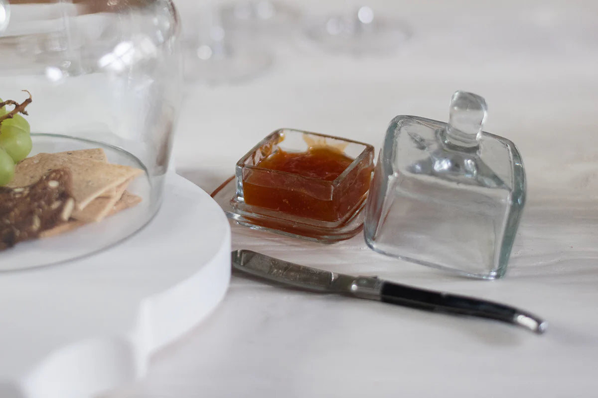 Glass jam jar with knife and crackers on a white surface