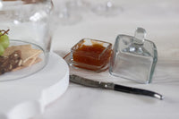 Glass jam jar with knife and crackers on a white surface