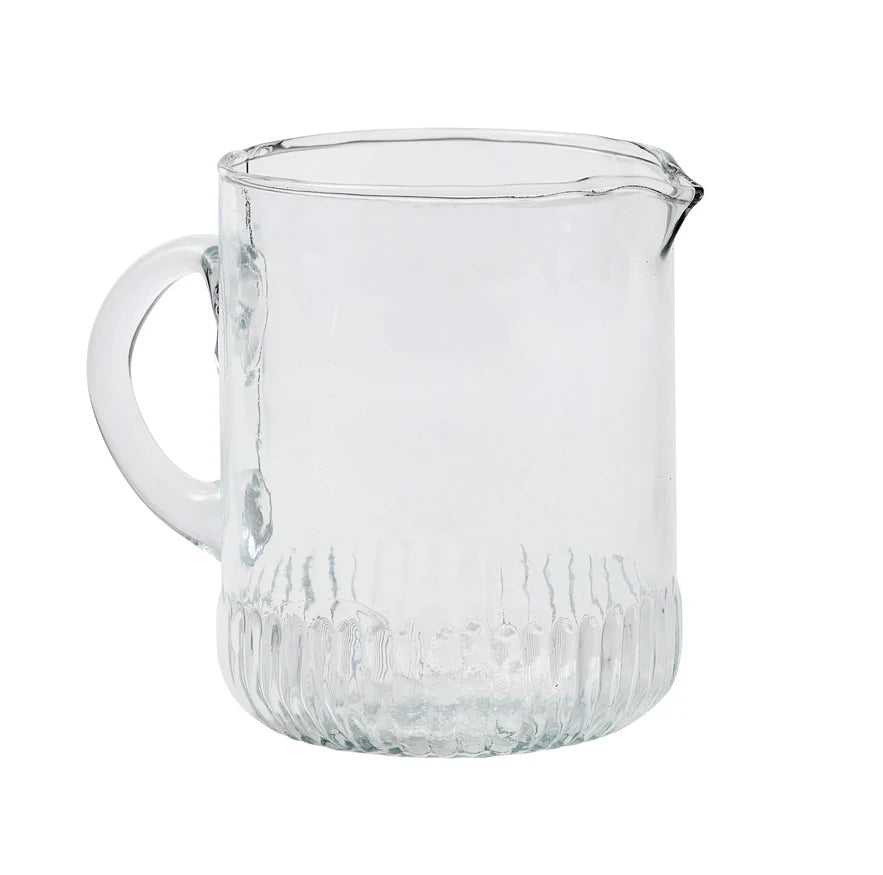 Clear glass pitcher with textured base on a white background
