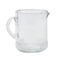 Clear glass pitcher with textured base on a white background