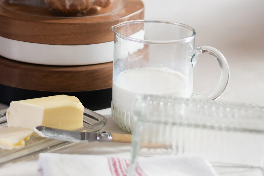 Glass pitcher of milk with a stick of butter on a wooden surface