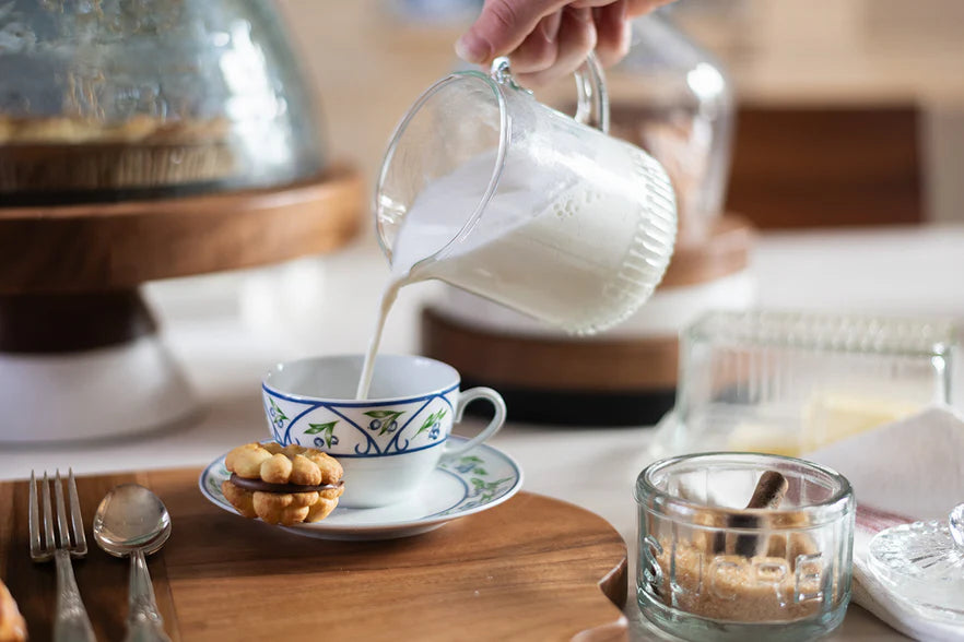 Person pouring milk into a teacup on a wooden table with a blurred background