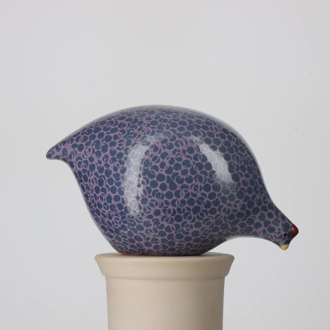 Ceramic pecking quail with blue and mauve pattern on a beige stand against a light gray background