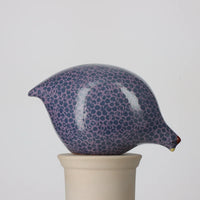 Ceramic pecking quail with blue and mauve pattern on a beige stand against a light gray background