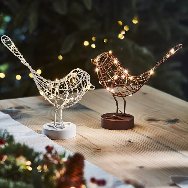 Decorative wire bird lights with string lights on a wooden surface with a festive background.