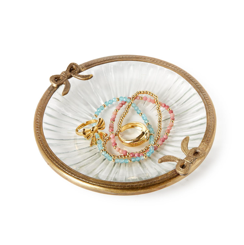 Jewelry dish with gold and pink rings and bracelets on a white background