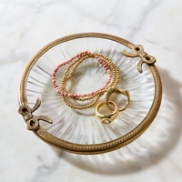 Gold jewelry on a decorative glass trinket tray with a marble background