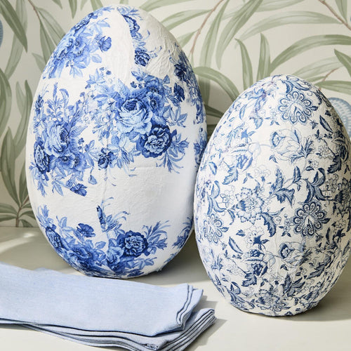 Two decorative eggs with blue floral patterns on a neutral background