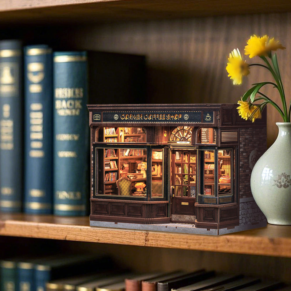Miniature model of a coffee shop on a bookshelf with books and a vase of flowers.