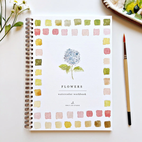 Watercolor workbook titled 'Flowers' by Emily Lex Studio on a white surface with a brush and flowers.