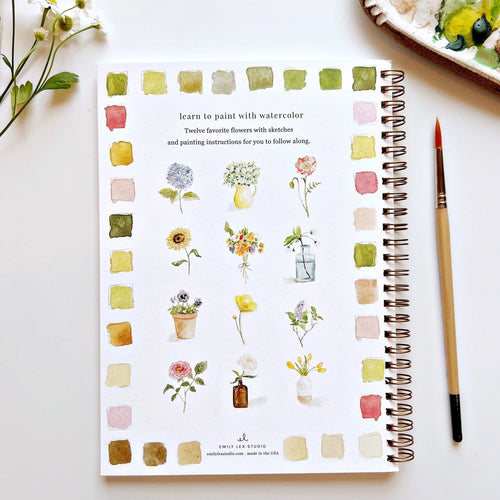 Notebook with watercolor flower illustrations and a paintbrush on a white surface