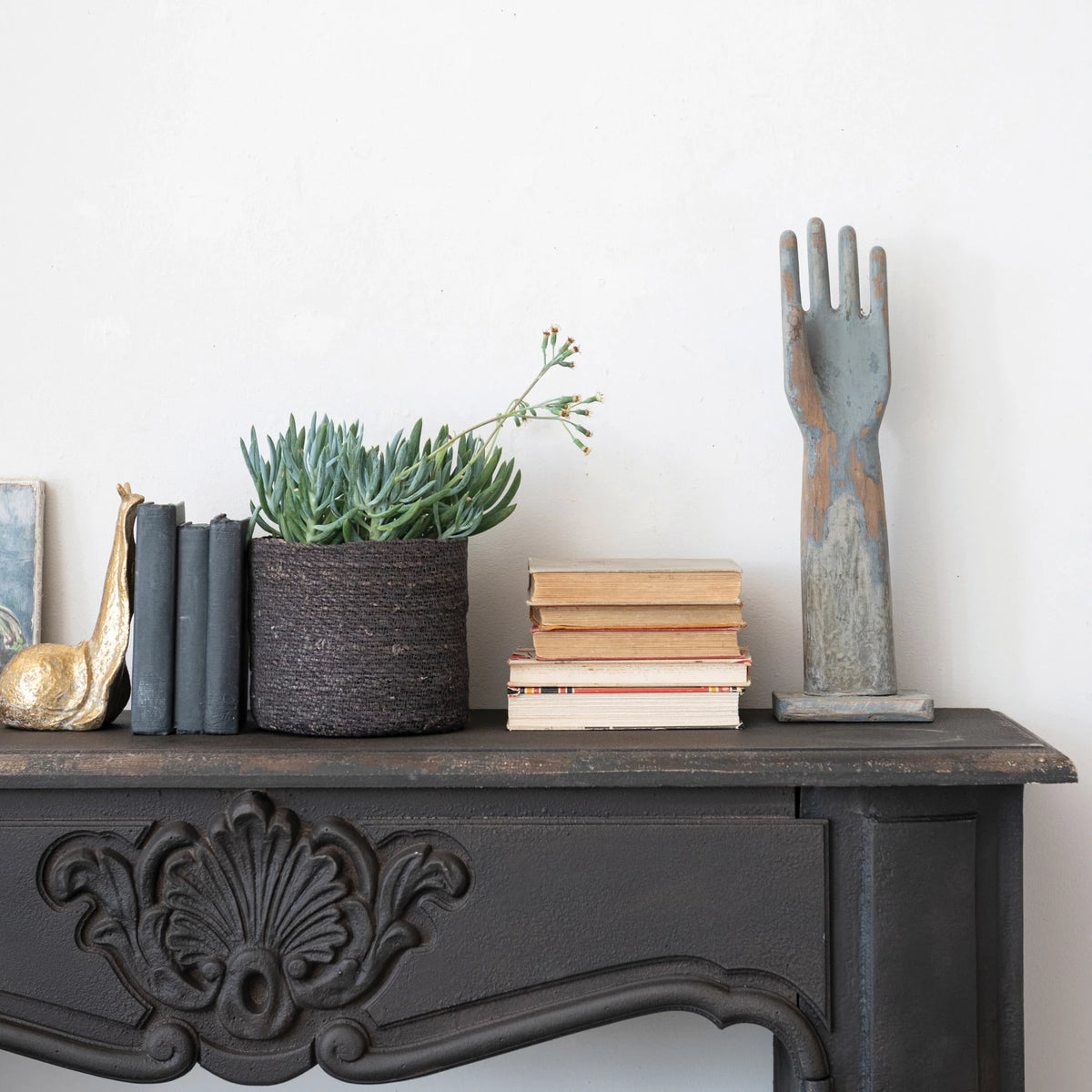 Decorative items on a mantelpiece including books, a plant, and a decorative hand sculpture.