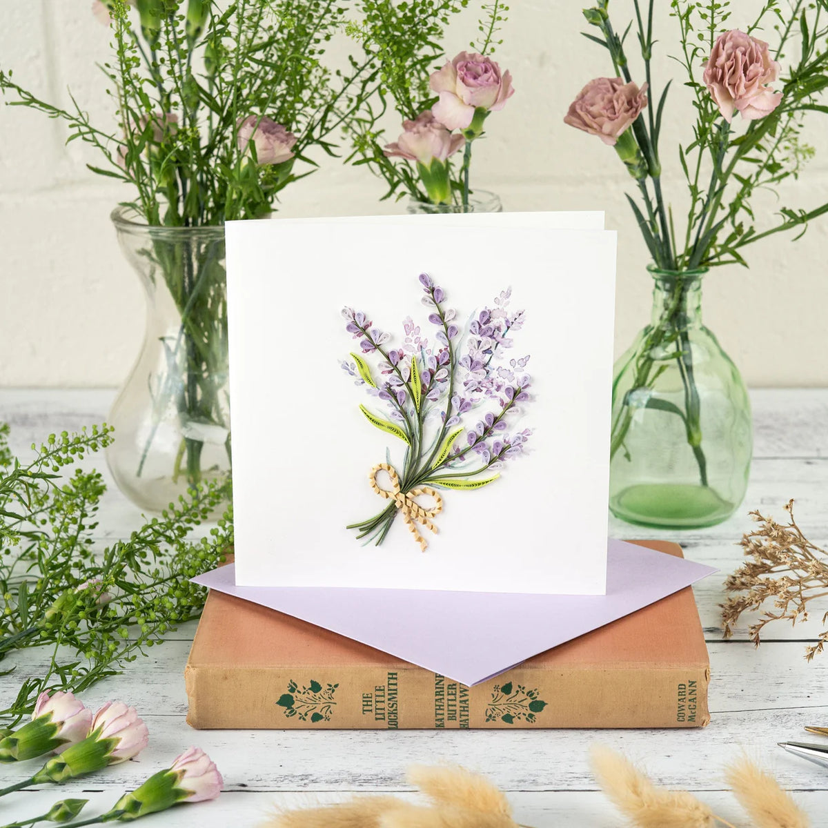 Floral card with lavender design on a stack of books with flowers in the background.