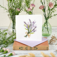 Floral card with lavender design on a stack of books with flowers in the background.
