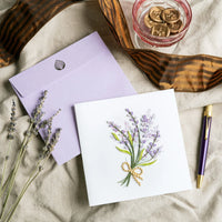 Greeting card with lavender design, purple envelope, and pen on textured surface