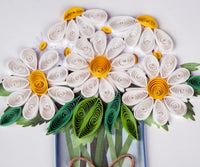 Quilled daisies with white petals, yellow centers, and green leaves on a white background.