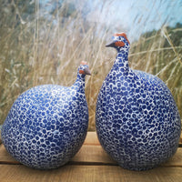 Two blue and white patterned ceramic birds on a wooden surface with a blurred natural background.