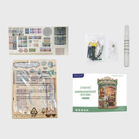 A collage of craft kit components on a light gray background, including a printed instruction sheet, small accessory packets, a white marker or paint tube, and a product box labeled 'Impressionist Studio' with 'The Book of Hooks' branding.