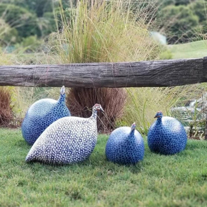 Decorative guinea fowl sculptures on grass with a wooden log and plants in the background