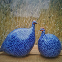 Two blue ceramic Guinea fowl with a circular pattern on a wooden surface with a grassy background.