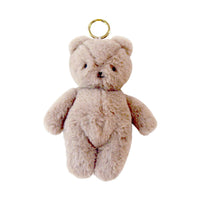 A small plush teddy bear keychain in a light beige or pale taupe color, featuring a gold metal ring at the top, set against a plain white background.