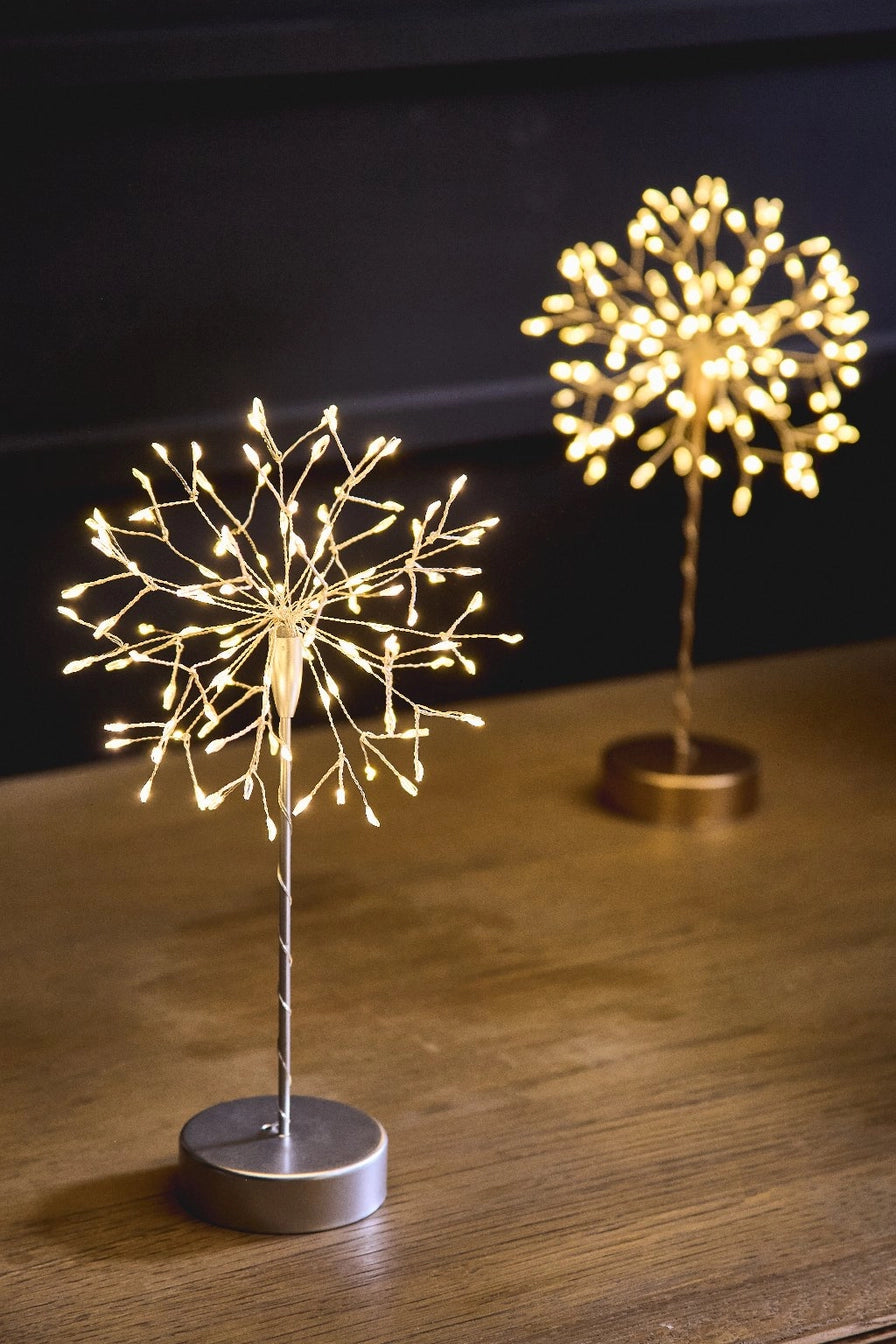 Two decorative LED light sculptures meant to mimic the look of a dandelion on a wooden surface with a dark background