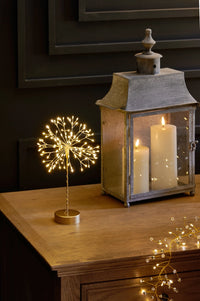 Decorative lantern with candles and a small lighted sculpture resembling a dandelion on a wooden surface.