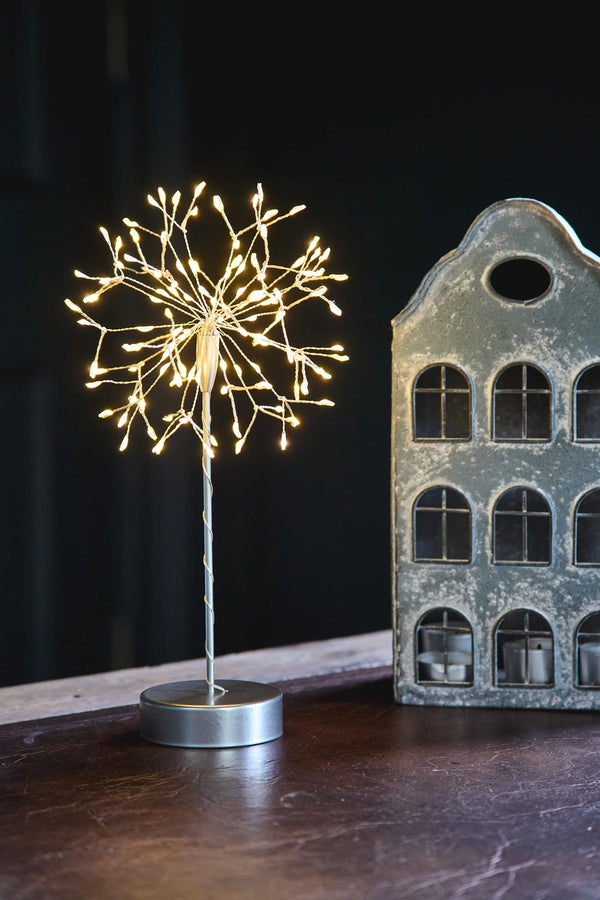 Decorative light fixture resembling a dandelion on a dark surface with a vintage-style building model in the background.