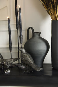 Decorative items including metal raven figures, candles, and a vase on a dark surface with a neutral background.