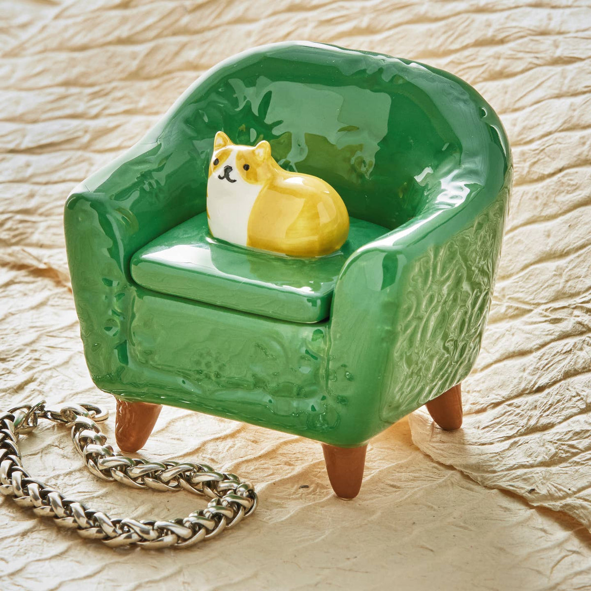 Green ceramic chair with an orange and white cat figurine on a textured beige surface