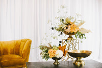 Decorative table setting with floral arrangements and gold bowls against a white curtain background.