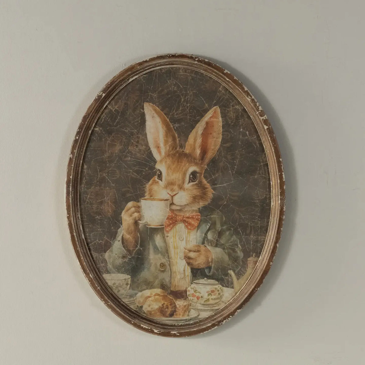 Decorative wall art of a rabbit holding a teacup in an oval frame.