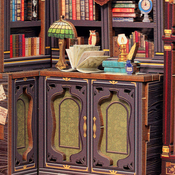 A miniature bookcase and cabinet unit in a detailed library setting, featuring dark wood panels with green patterned glass doors, surrounded by miniature books, a stained-glass lamp, an open book, and a small owl figurine.