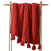 Red knitted blanket with tassels on a wooden stand against a white background