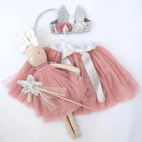 A fairy-themed outfit set featuring a dusty pink tutu skirt with a white satin bow, a matching pink tutu dress on a bunny doll, a silver glitter bunny crown, and a silver glitter star wand, all arranged on a white background.