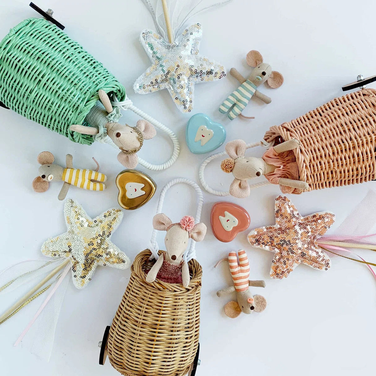 A styled flat-lay of mouse plushies and wands with sequin star tops, with wicker baskets, and tooth fairy tooth containers on a white background.