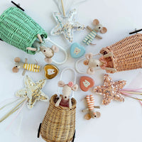 A styled flat-lay of mouse plushies and wands with sequin star tops, with wicker baskets, and tooth fairy tooth containers on a white background.