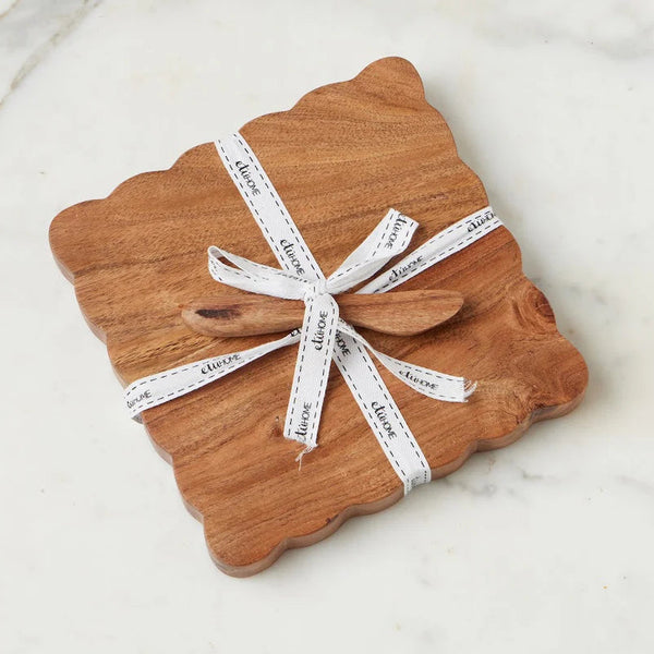 Brown scalloped cheese board wrapped in white ribbon on a marble surface
