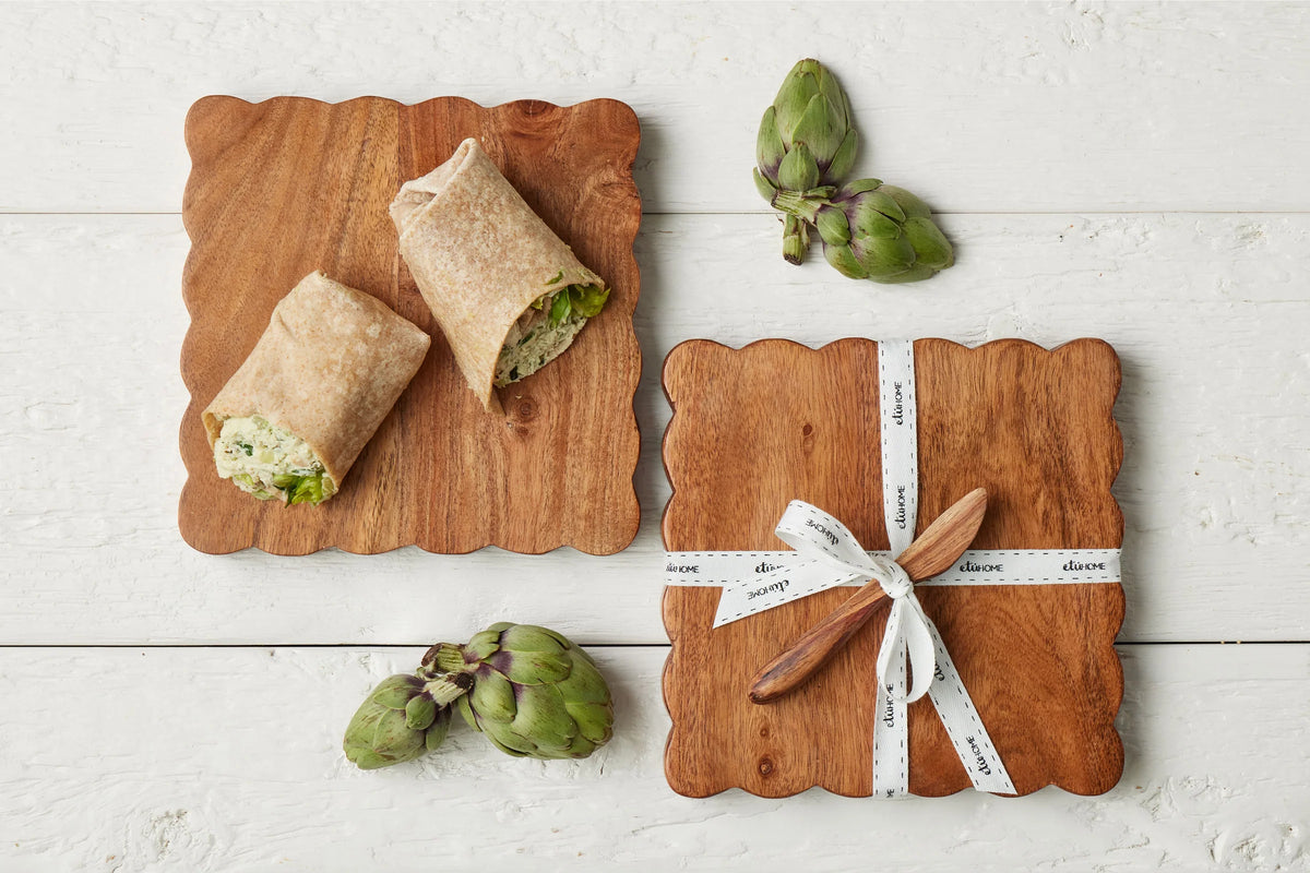 Two wraps on a wooden cutting board with artichokes and a knife set on a white wooden surface.