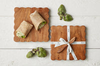 Two wraps on a wooden cutting board with artichokes and a knife set on a white wooden surface.