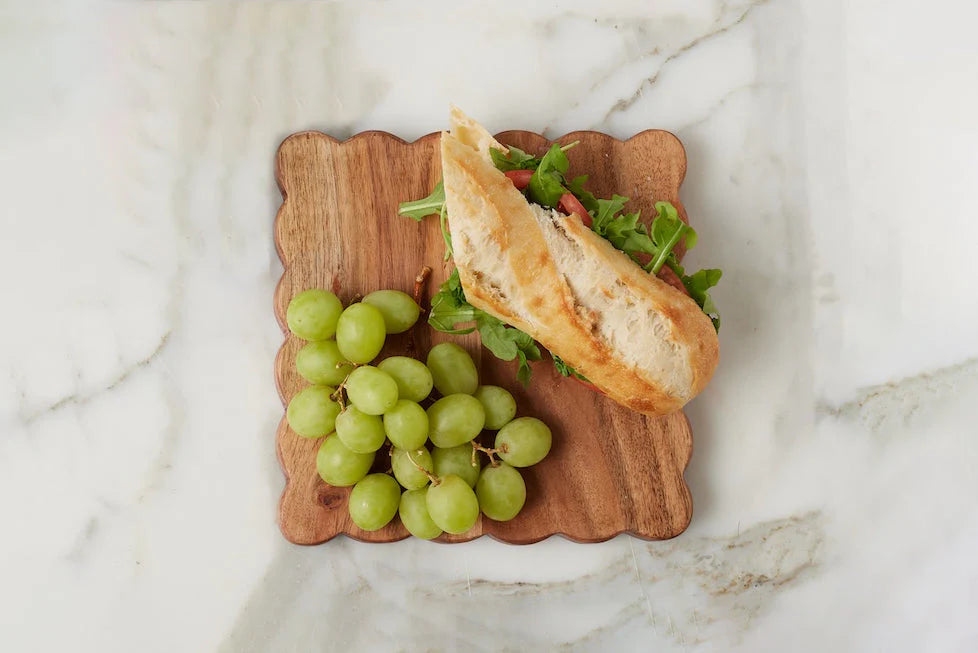 Small sandwich with greens and a side of grapes on a wooden board over a marble background