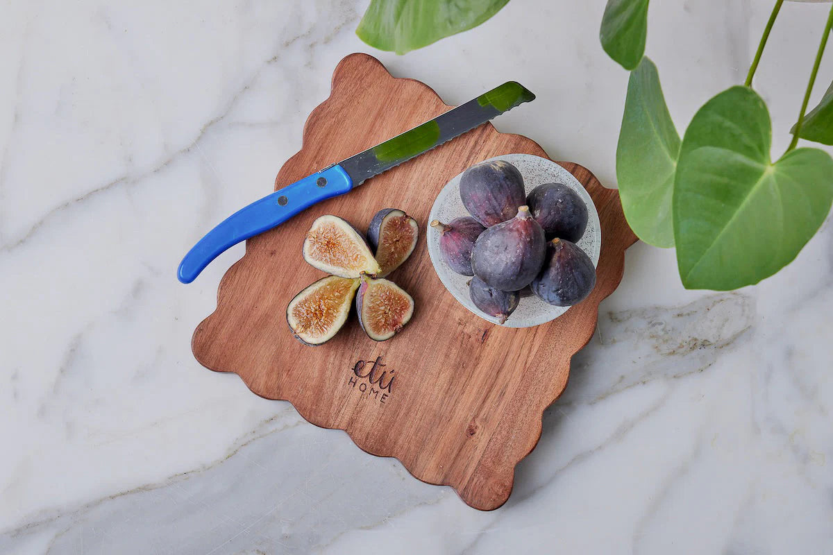 Wooden cheese board with sliced figs and a knife on a marble surface